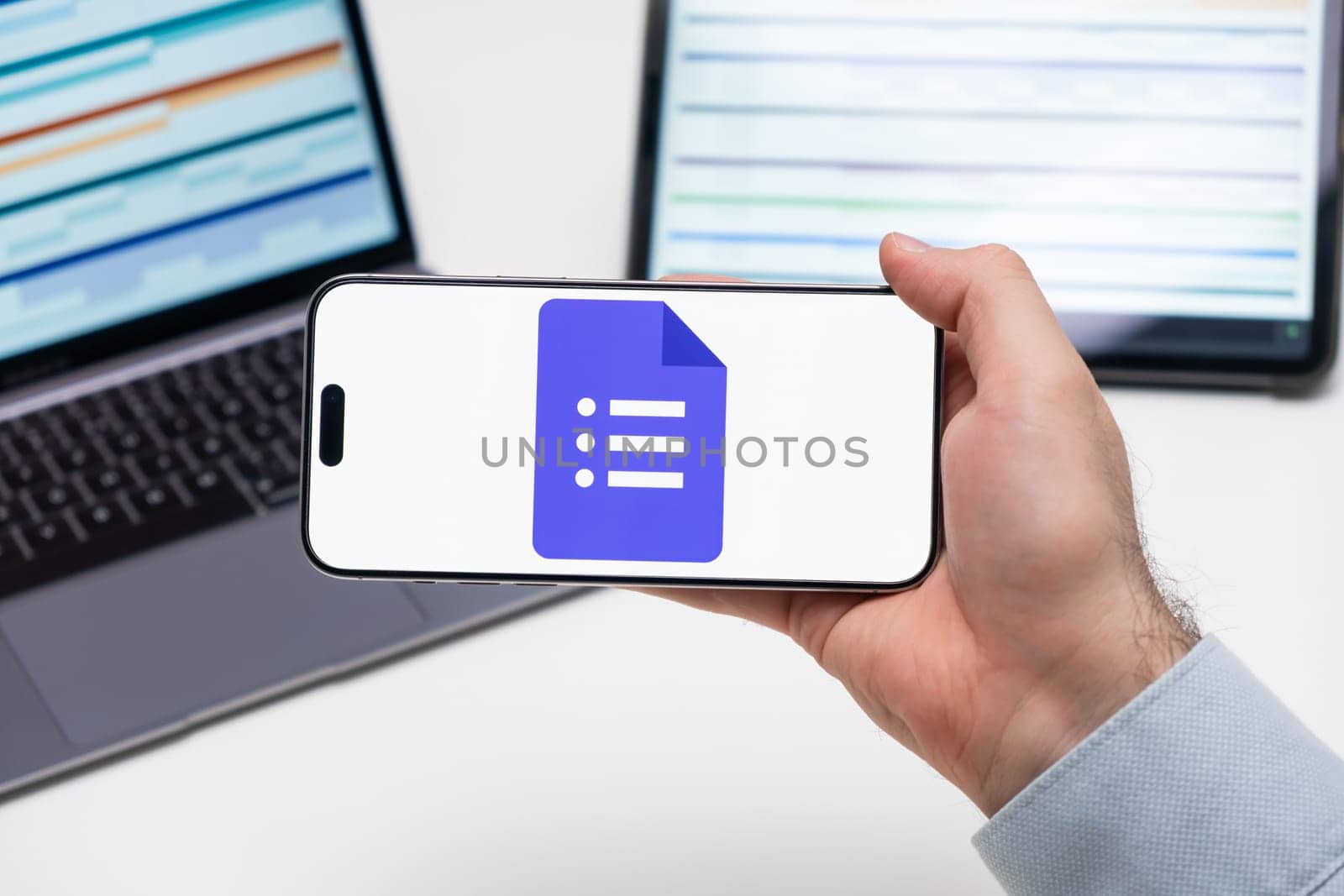 PRAGUE, CZECH REPUBLIC - JANUARY 21 2024:Google Docs logo on the screen of a cell phone in business mans hand and laptop on the background.