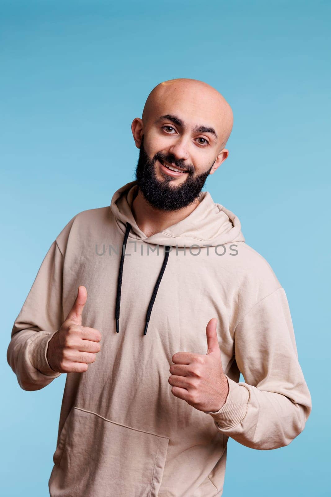 Cheerful arab man showing approval gesture with two thumbs up portrait. Smiling person with joyful facial expression standing with satisfaction sign while looking at camera