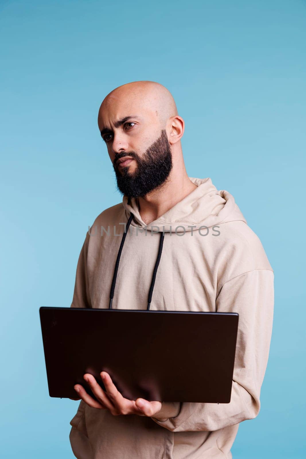 Puzzled arab man programming on laptop and looking away with confused expression. Confused person in doubt while developing software app and writing code on portable computer