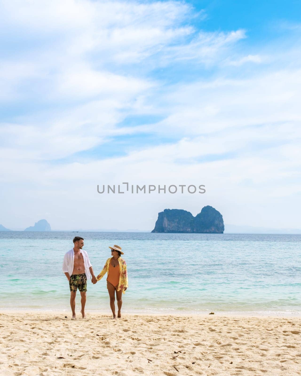 Happy young couple, an Asian woman and European man on the beach of Koh Ngai island, soft white sand, and a turqouse colored ocean in Koh Ngai Trang Thailand