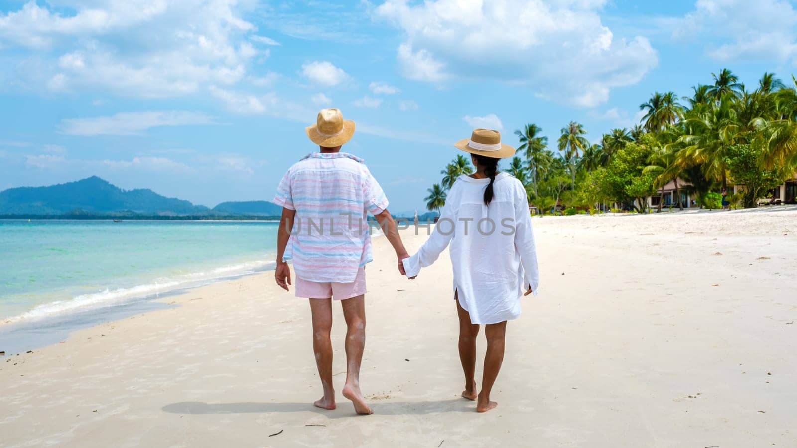 Koh Mook a young couple of caucasian men and Thai Asian woman walking at the beach in Thailand by fokkebok