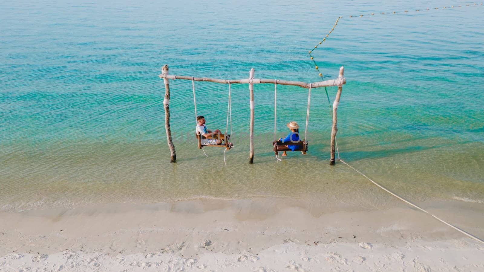 a couple of men and a woman on a swing at the beach of Koh Muk, a tropical island and a turqouse colored ocean in Koh Mook Trang Thailand, a couple on a swing in the ocean