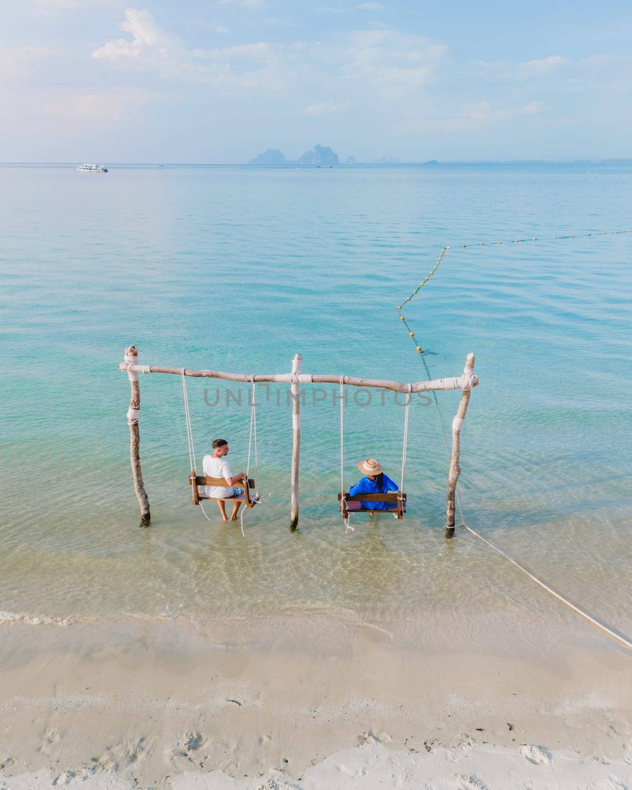 a couple of men and a woman on a swing at the beach of Koh Muk, a tropical island and a turqouse colored ocean in Koh Mook Trang Thailand, a couple on a swing in the ocean