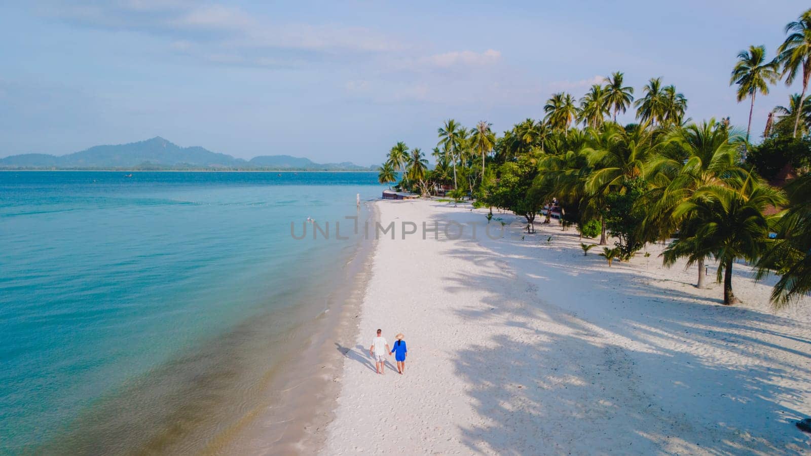 Top view at a couple walking on the white sandy tropical beach of Koh Muk with palm trees soft white sand, and a turqouse colored ocean in Koh Mook Trang Thailand