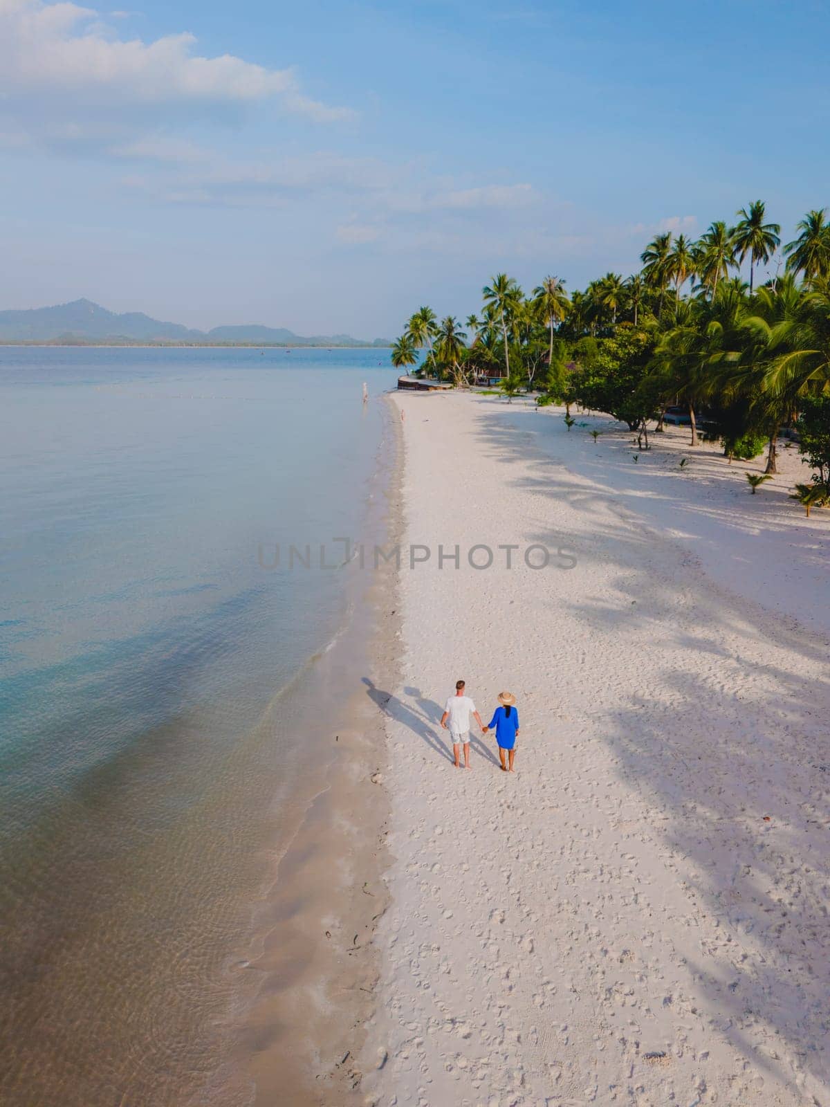 Top view at a couple walking on the white sandy tropical beach of Koh Muk with palm trees soft white sand, and a turqouse colored ocean in Koh Mook Trang Thailand