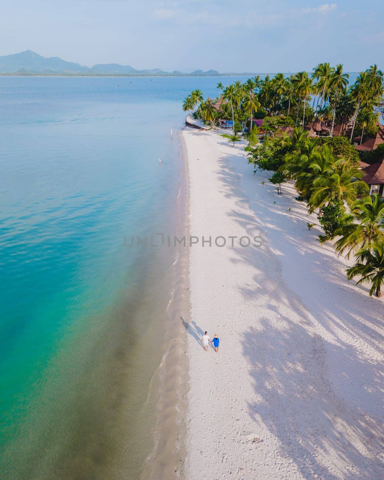 Top view at a couple walking on the white sandy tropical beach of Koh Muk with palm trees soft white sand, and a turqouse colored ocean in Koh Mook Trang Thailand