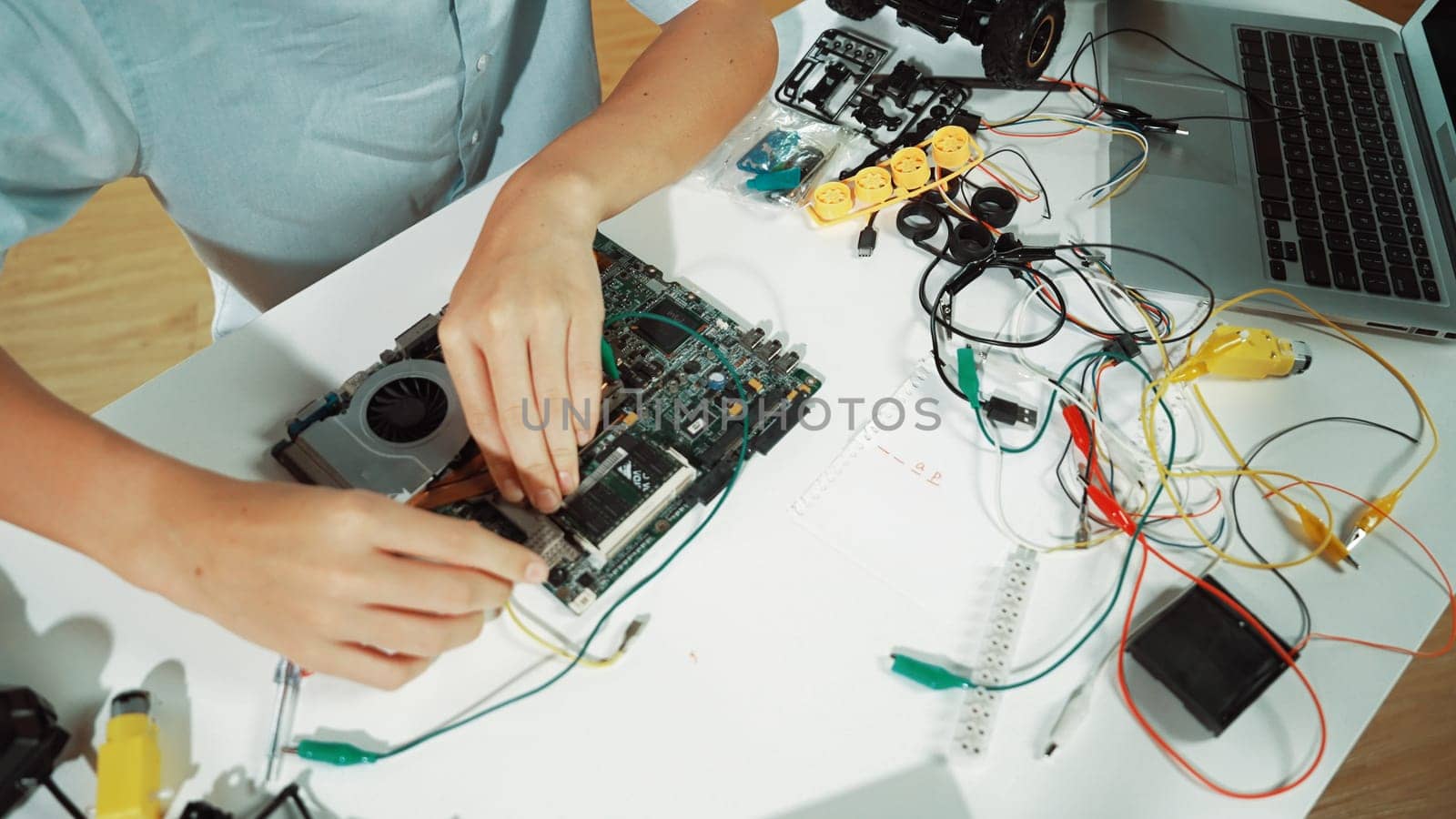 Closeup of boy hand fixing motherboard with electronic tool on table. Top view of highschool student repair electric board with electronic equipment, wires tool scatter around on table. Edification.