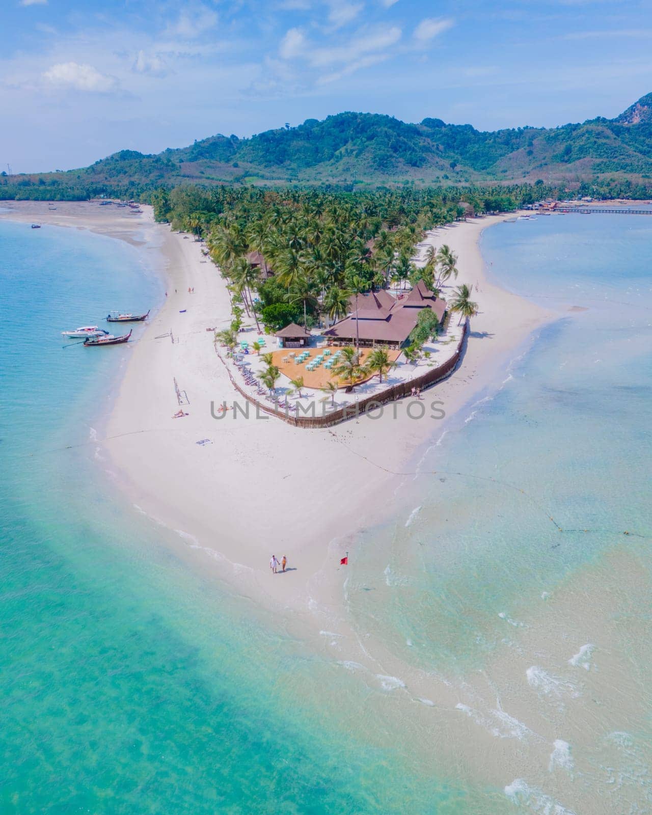 Drone aerial view at Koh Muk a tropical island with palm trees soft white sand, and a turqouse colored ocean in Koh Mook Trang Thailand, a couple on a sandbar in the ocean on a sunny day