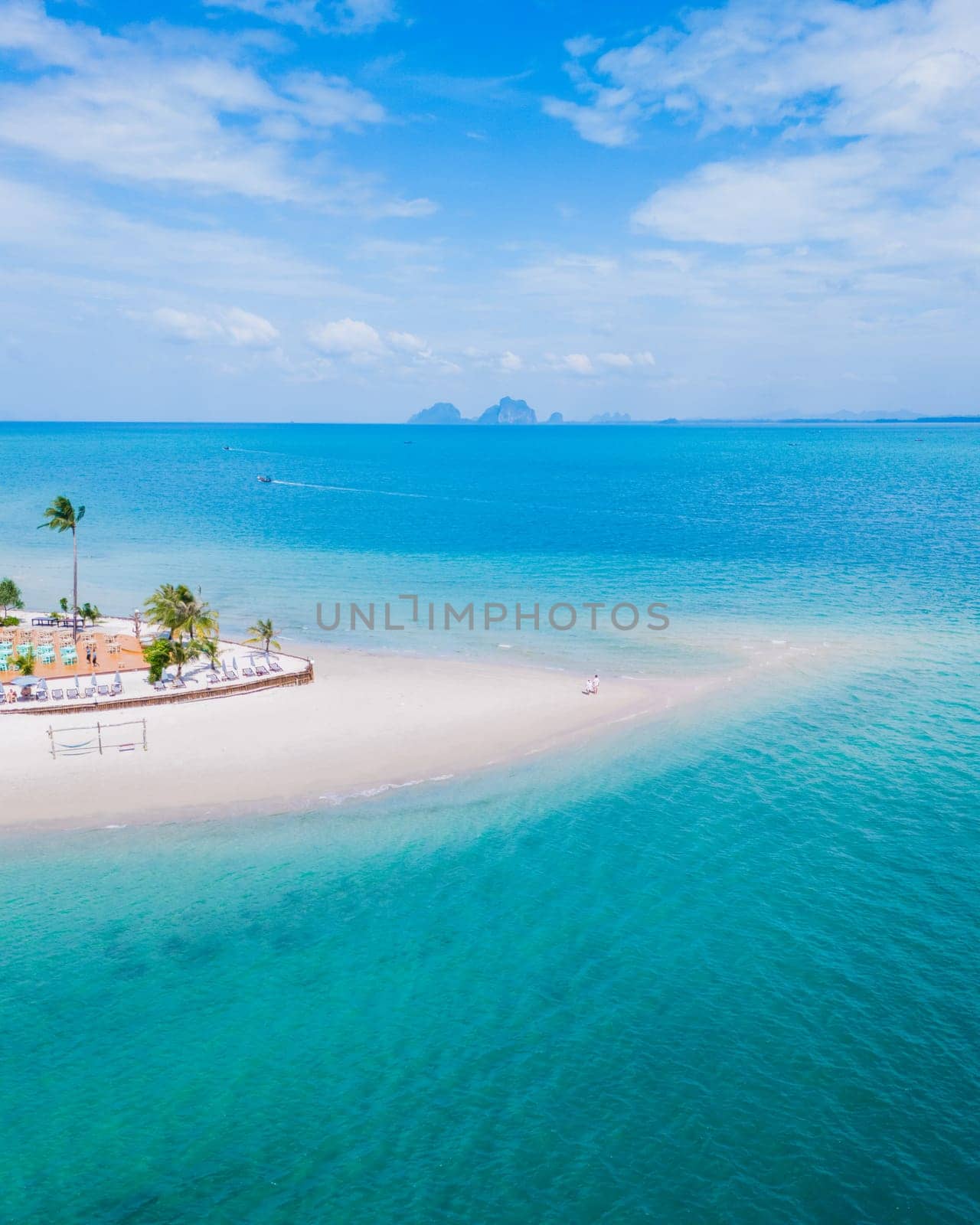 Drone aerial view at Koh Muk a tropical island with palm trees soft white sand, and a turqouse colored ocean in Koh Mook Trang Thailand, a couple on a sandbar in the ocean on a sunny day