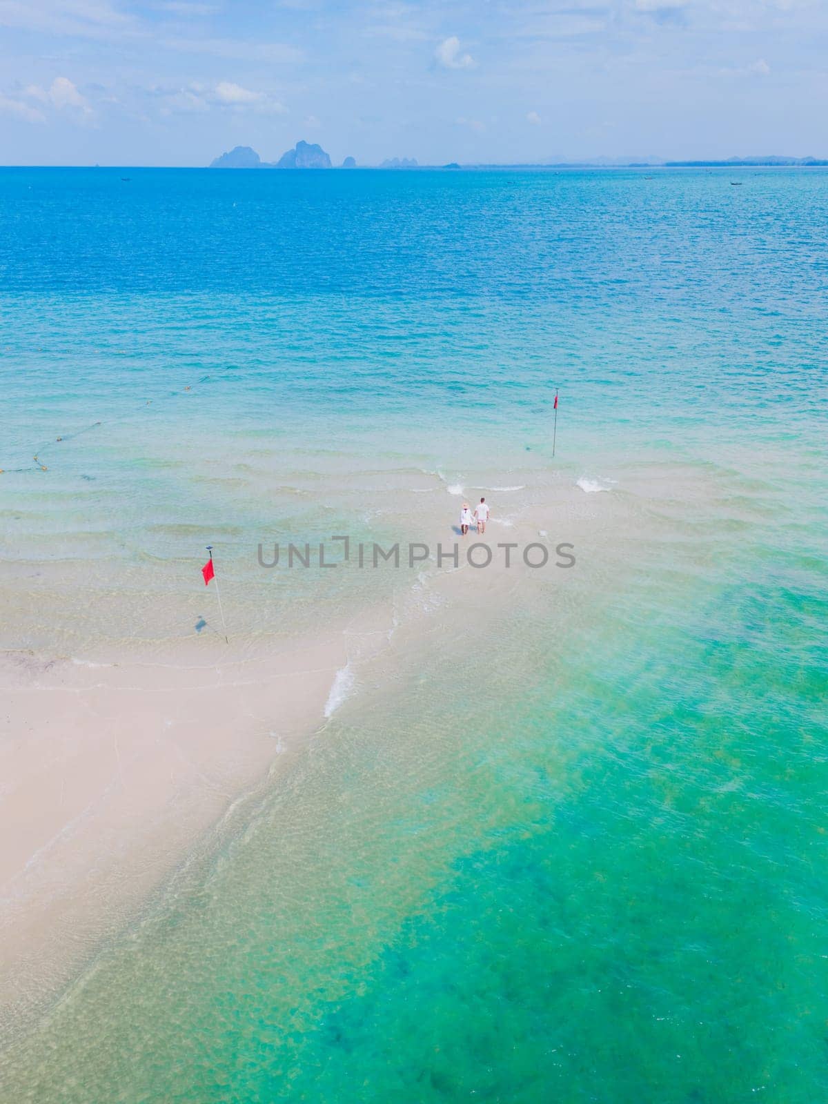 a couple of men and woman walking at a sandbar in the ocean of Koh Muk a tropical island with palm trees and soft white sand, and a turqouse colored ocean in Koh Mook Trang Thailand