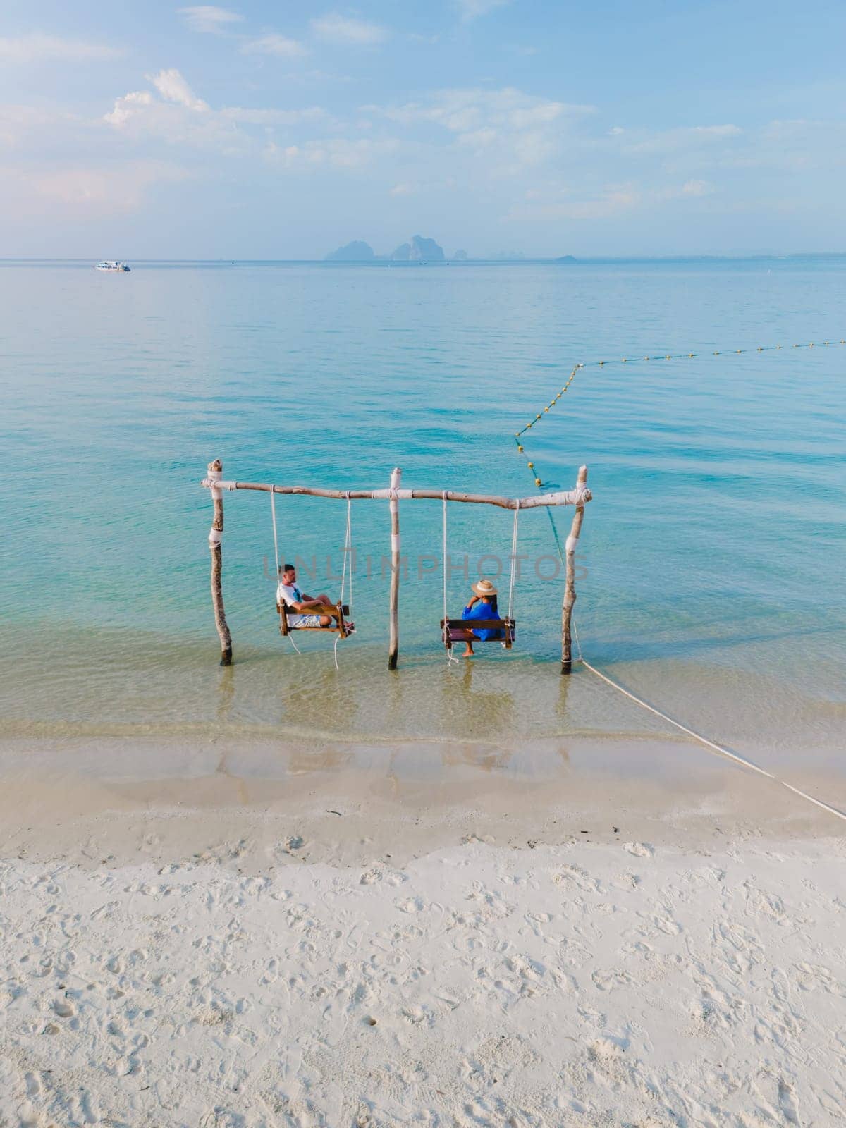 a couple of men and a woman on a swing at the beach of Koh Muk tropical island , and a turqouse colored ocean in Koh Mook Trang Thailand, a couple on a swing in the ocean