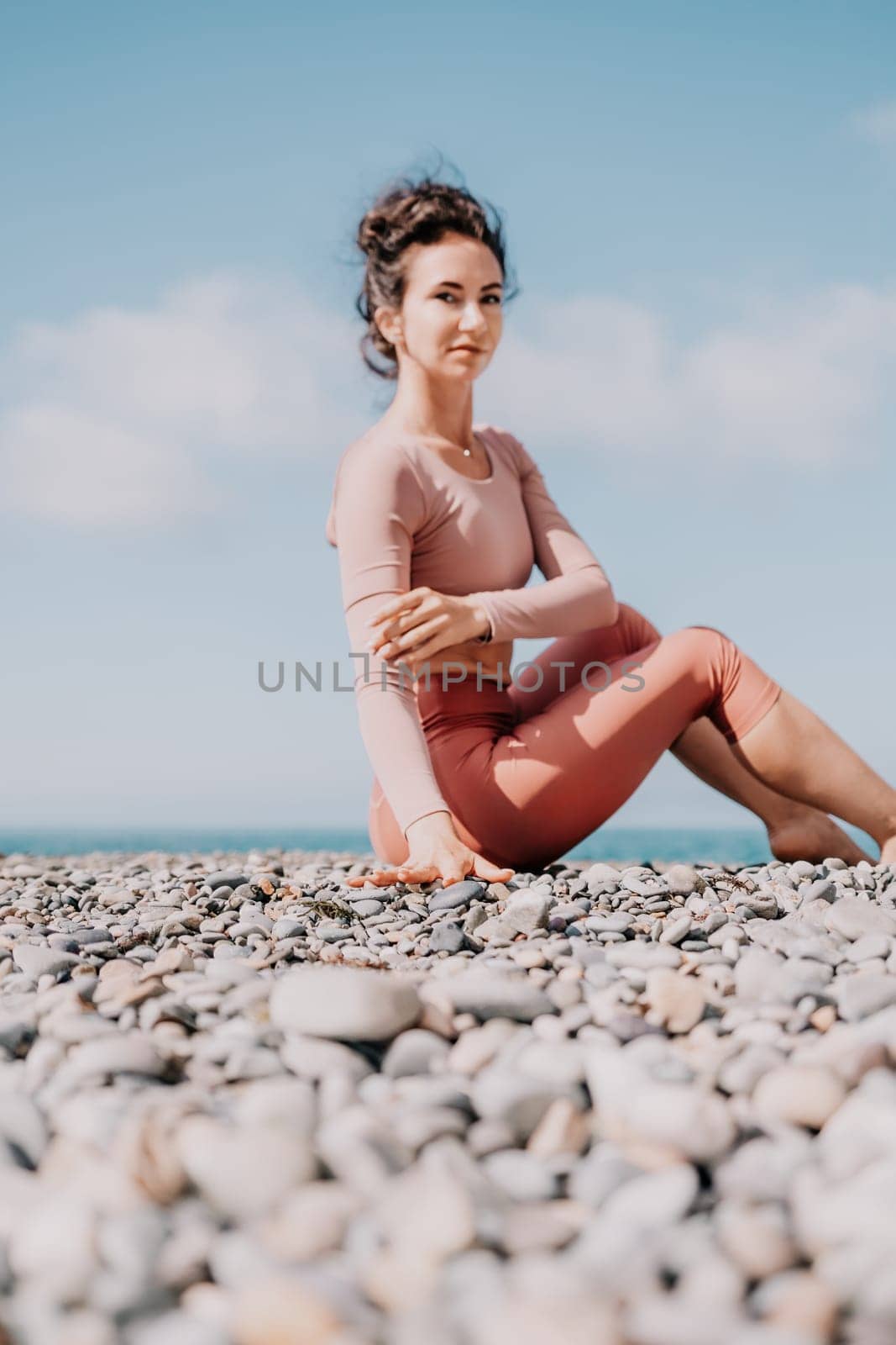 Young woman with long hair in white swimsuit and boho style braclets practicing outdoors on yoga mat by the sea on a sunset. Women's yoga fitness routine. Healthy lifestyle, harmony and meditation