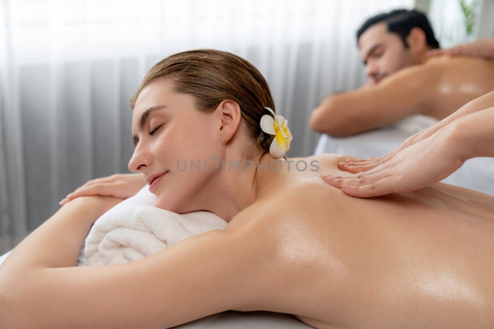 Caucasian couple customer enjoying relaxing anti-stress spa massage and pampering with beauty skin recreation leisure in day light ambient salon spa at luxury resort or hotel. Quiescent