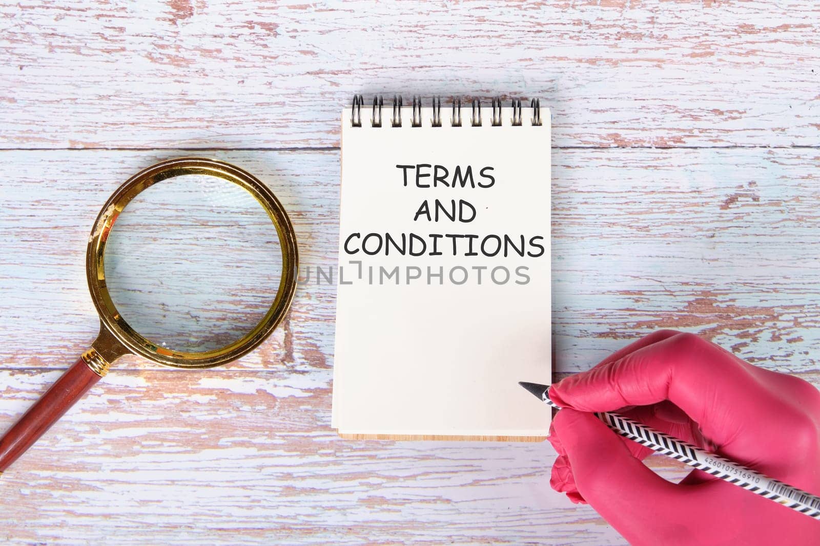 TERMS AND CONDITIONS writing on a notebook lying on old boards next to a magnifying glass and a hand in a red medical glove with a pencil