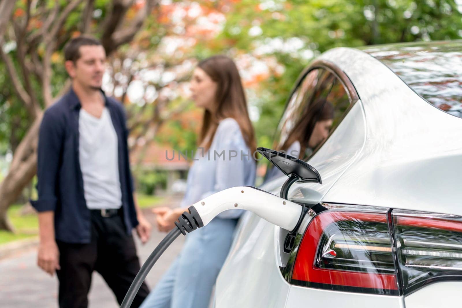 Lovely young couple recharging battery for electric car during autumnal road trip travel EV car in autumnal forest. Eco friendly travel on vacation during autumn. Exalt