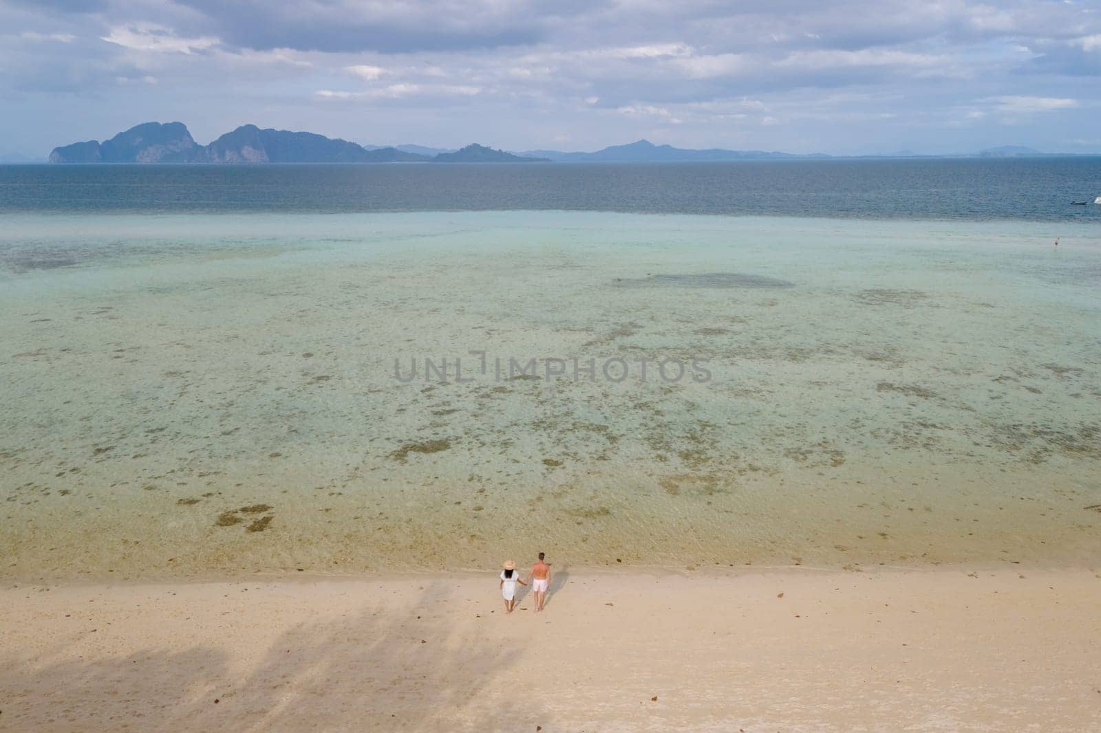oh Kradan a tropical island with palm trees soft white sand, and a turqouse colored ocean, couple standing by the ocean in Koh Kradan Trang Thailand