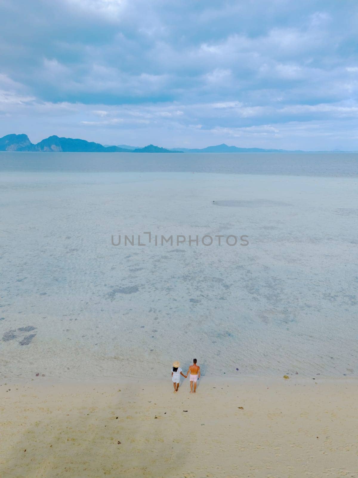 oh Kradan a tropical island with palm trees soft white sand, and a turqouse colored ocean, couple standing by the ocean in Koh Kradan Trang Thailand