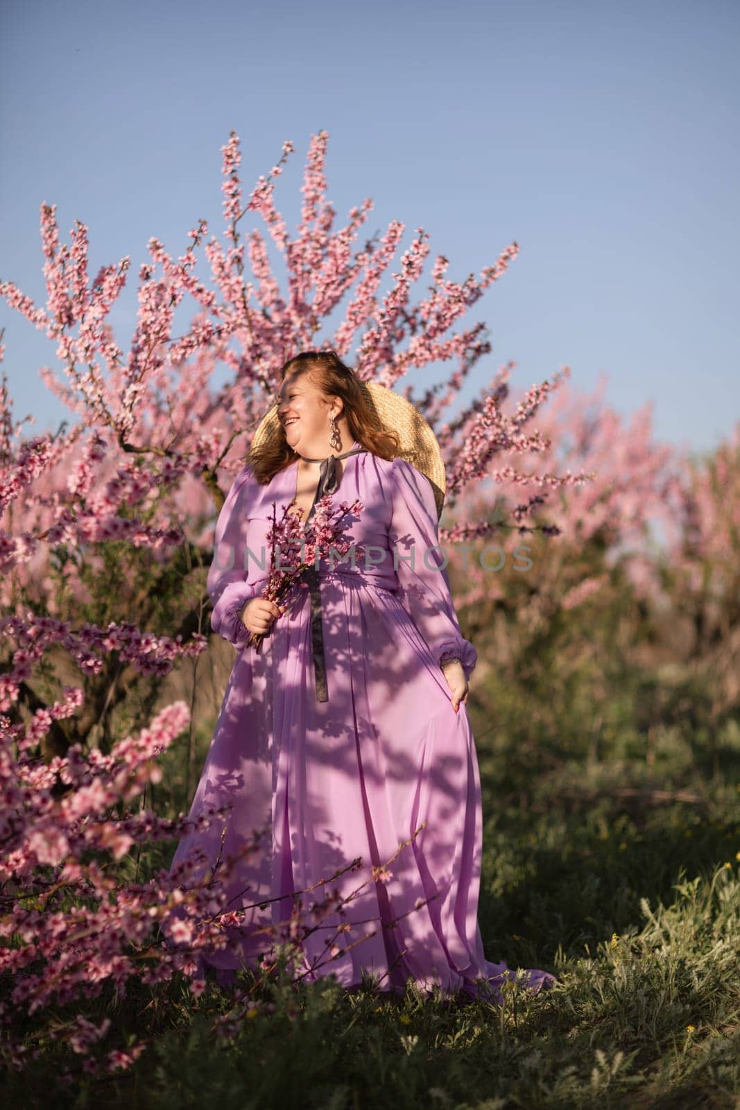 Woman blooming peach orchard. Against the backdrop of a picturesque peach orchard, a woman in a long pink dress and hat enjoys a peaceful walk in the park, surrounded by the beauty of nature. by Matiunina