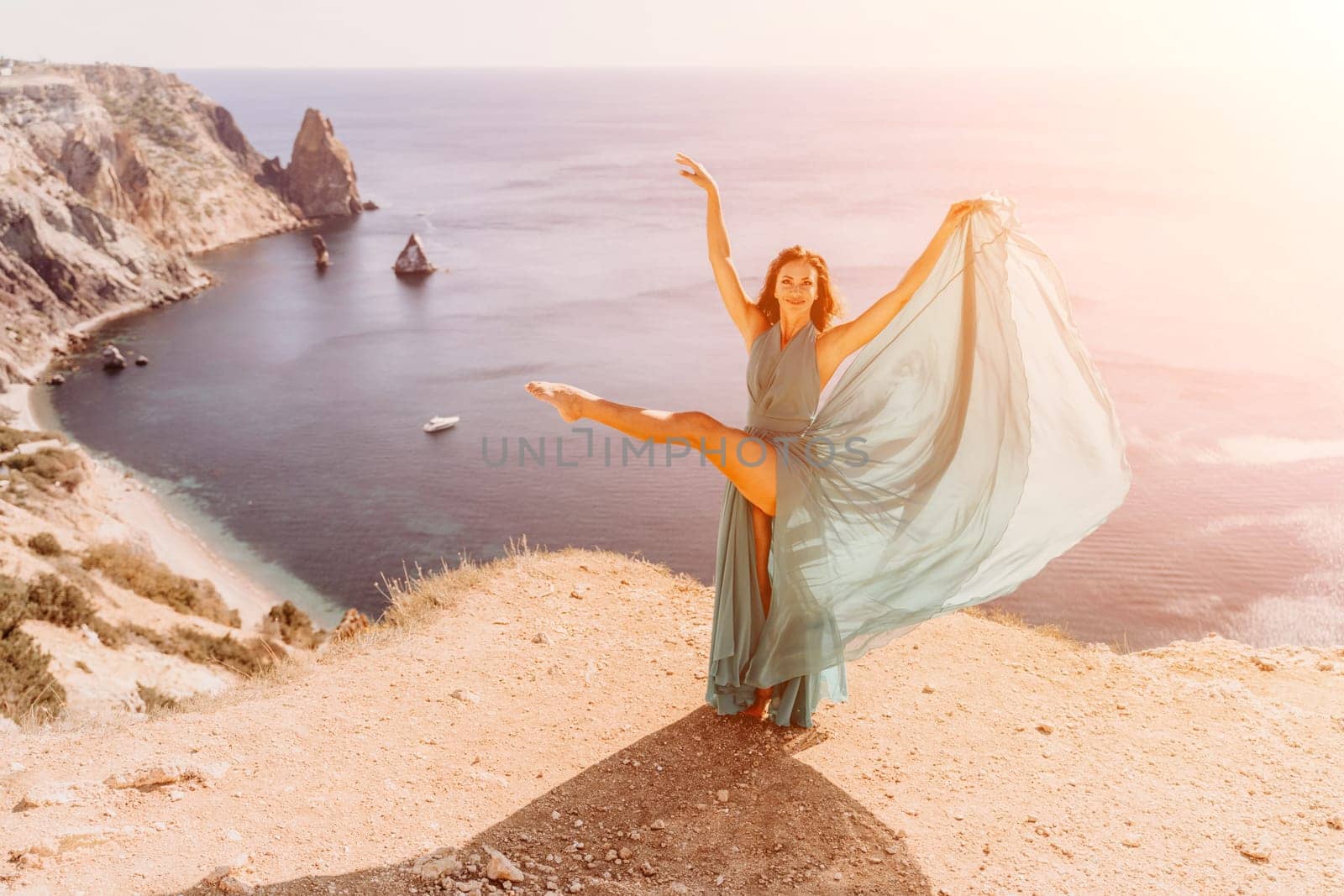 Woman green dress sea. Female dancer posing on a rocky outcrop high above the sea. Girl on the nature on blue sky background. Fashion photo