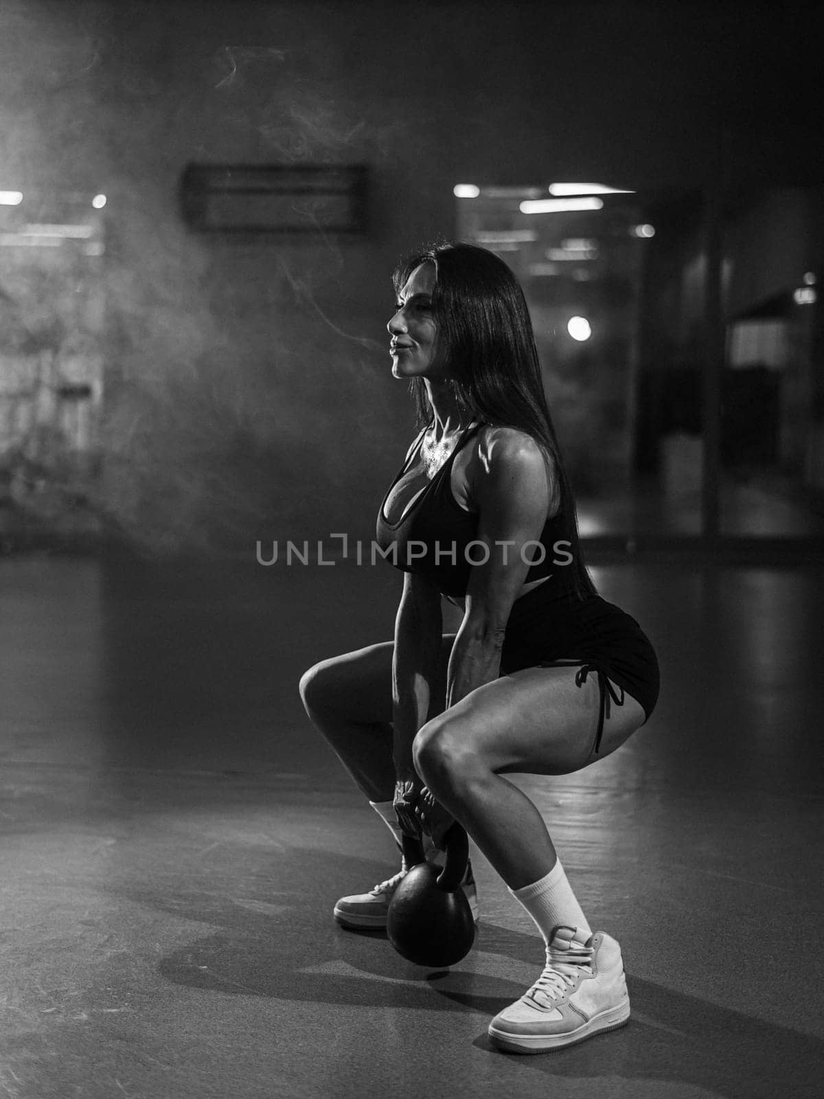 Caucasian woman squats with a kettlebell in the gym. Vertical photo. by mrwed54
