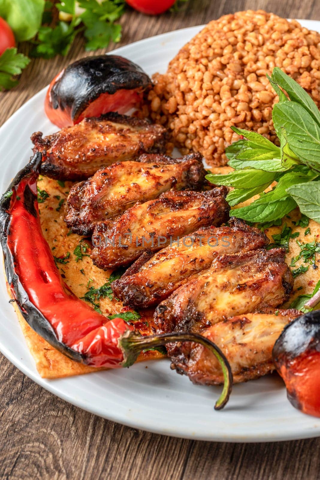 Barbecue chicken wings garnished with bulgur pilaf, roasted peppers and tomatoes. Traditional Turkish chicken wings by Sonat
