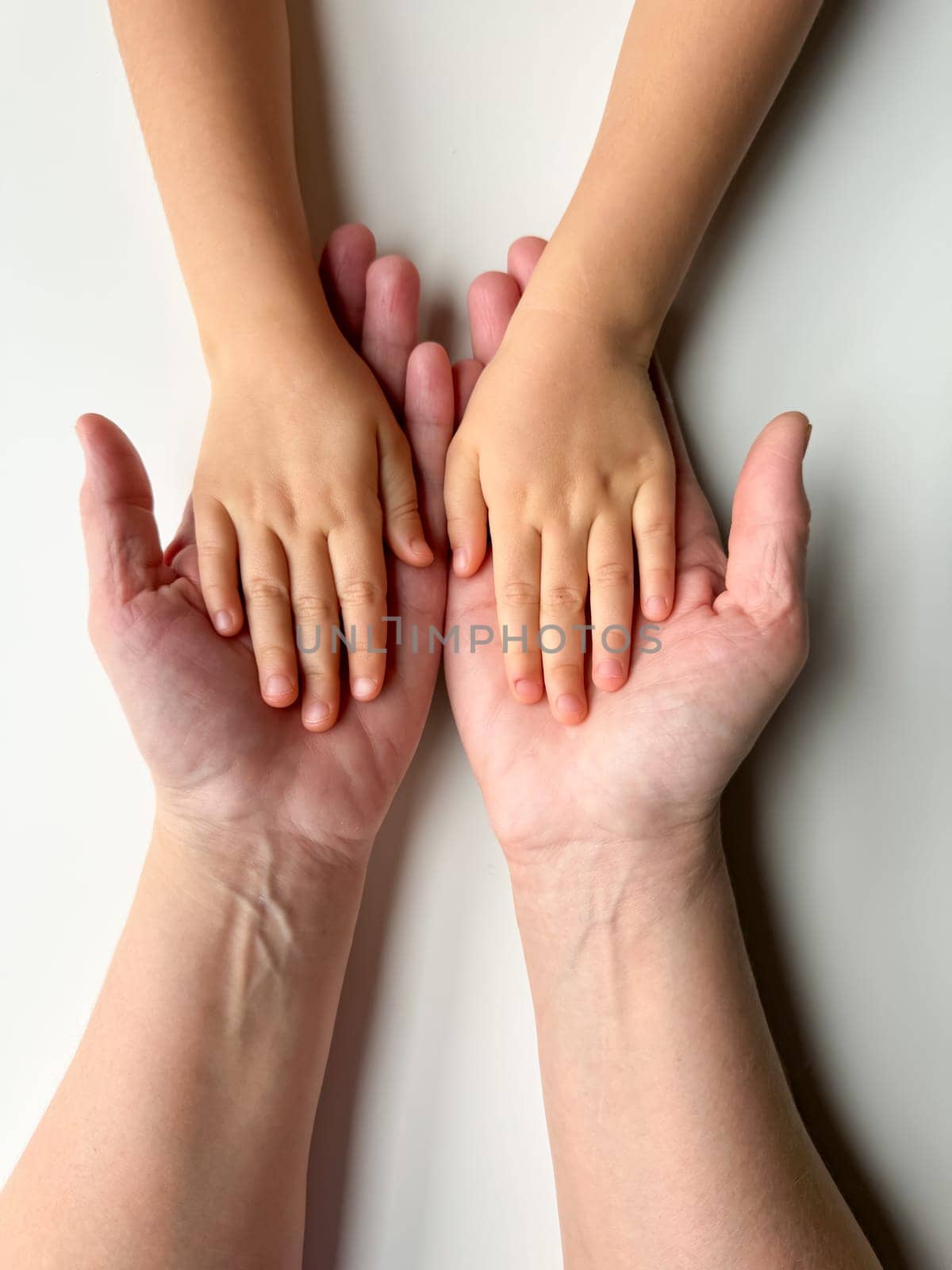 Mothers hands holding childs hands on white background. by Lunnica