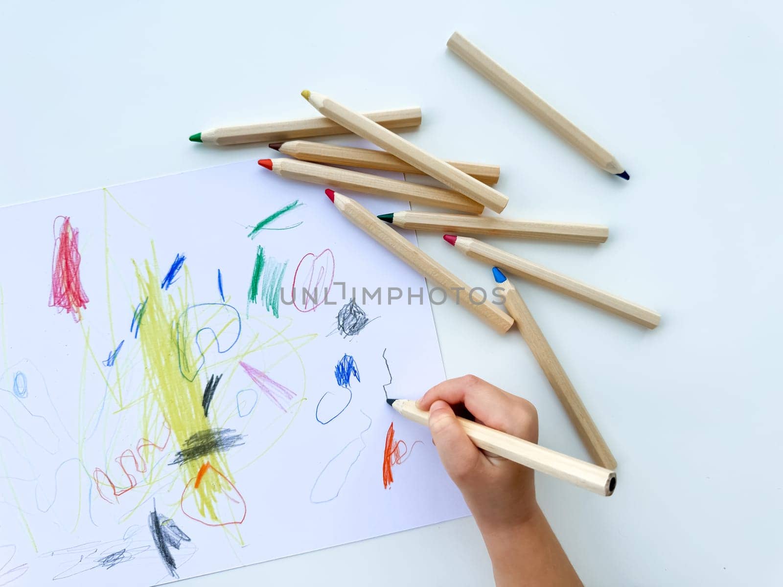 small child draws with colored pencils on paper on white table. High quality photo