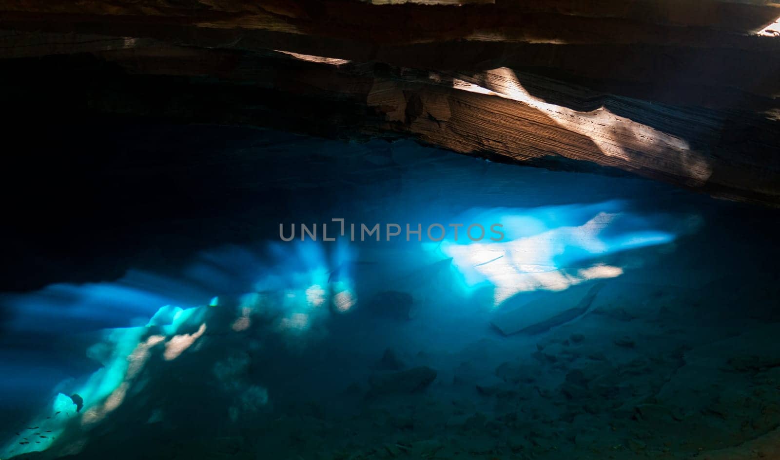 Sunlight streams through a cave, lighting up the blue waters beneath.
