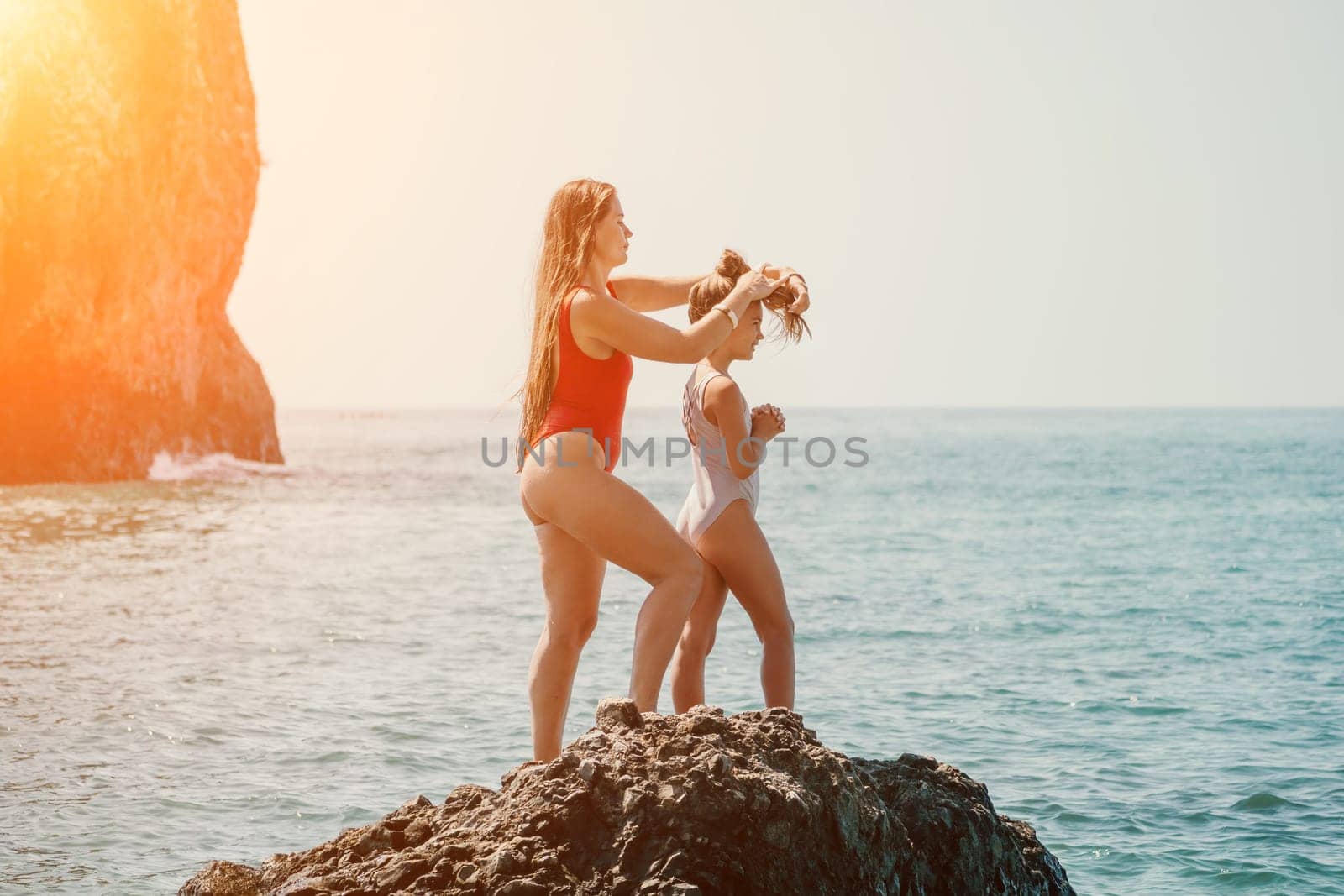 Woman and her daughter together on rock in the sea. Silhouette mother and daughter doing yoga at beach by panophotograph