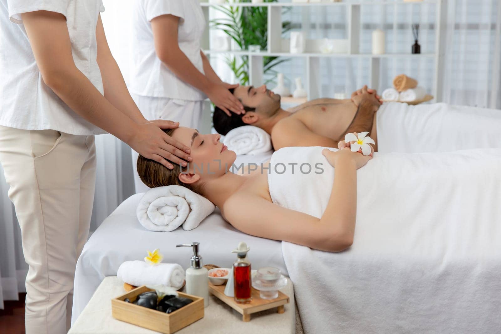 Caucasian couple enjoying relaxing anti-stress head massage and pampering facial beauty skin recreation leisure in dayspa modern light ambient at luxury resort or hotel spa salon. Quiescent
