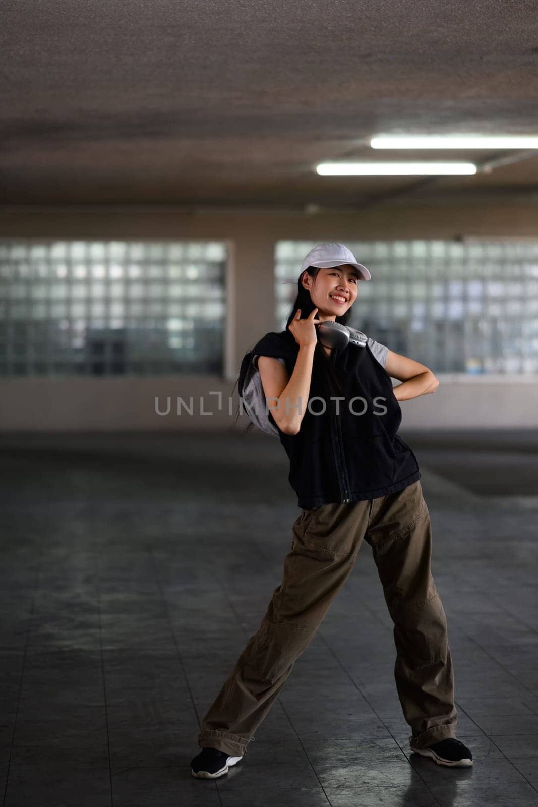 Full length of smiling young woman wearing visor cap dancing in underground car parking.