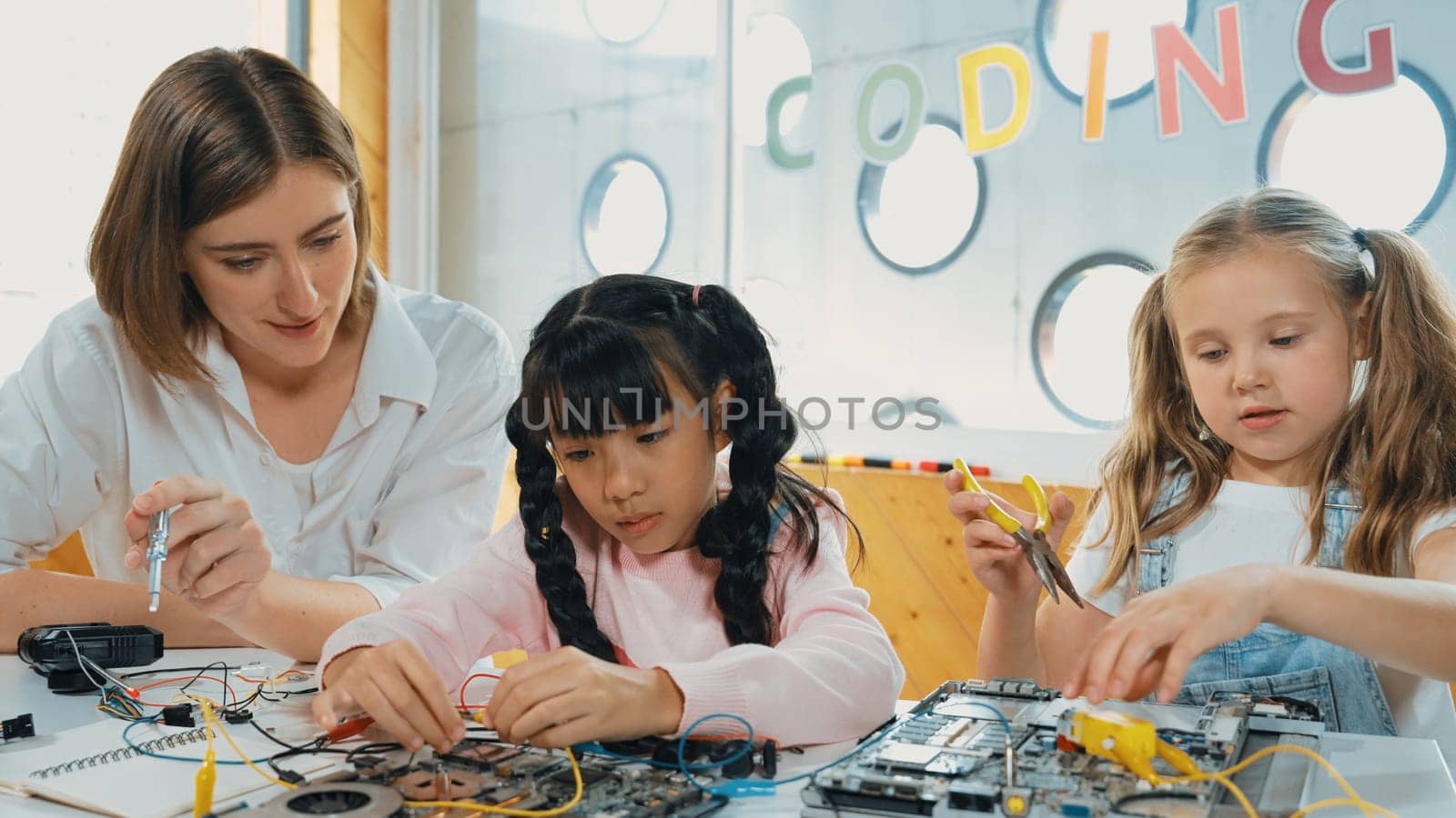 Skilled caucasian teacher teach and explain students about digital electrical tool. Expert girl learn electronic equipment and use to fix motherboard at table with chips and wires placed. Erudition.