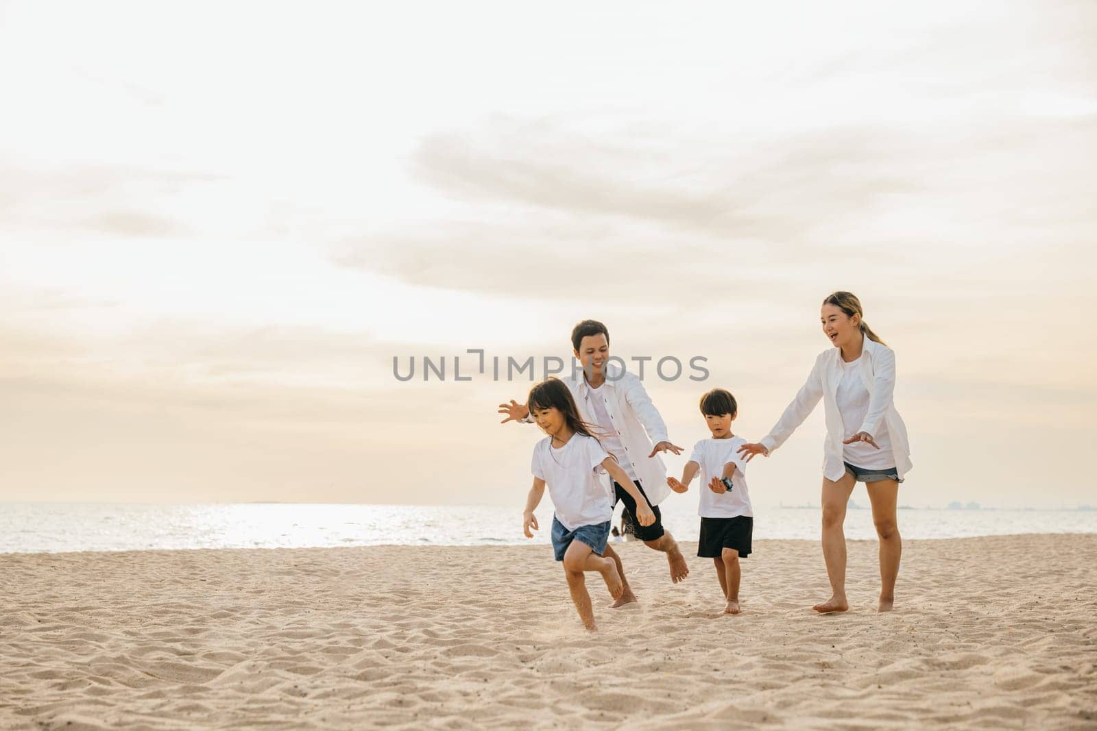 Smiling father and mother with son and daughter enjoying a carefree beach day. Running playing and laughing together creating memories of happiness family time and vitality. Family on beach vacation by Sorapop