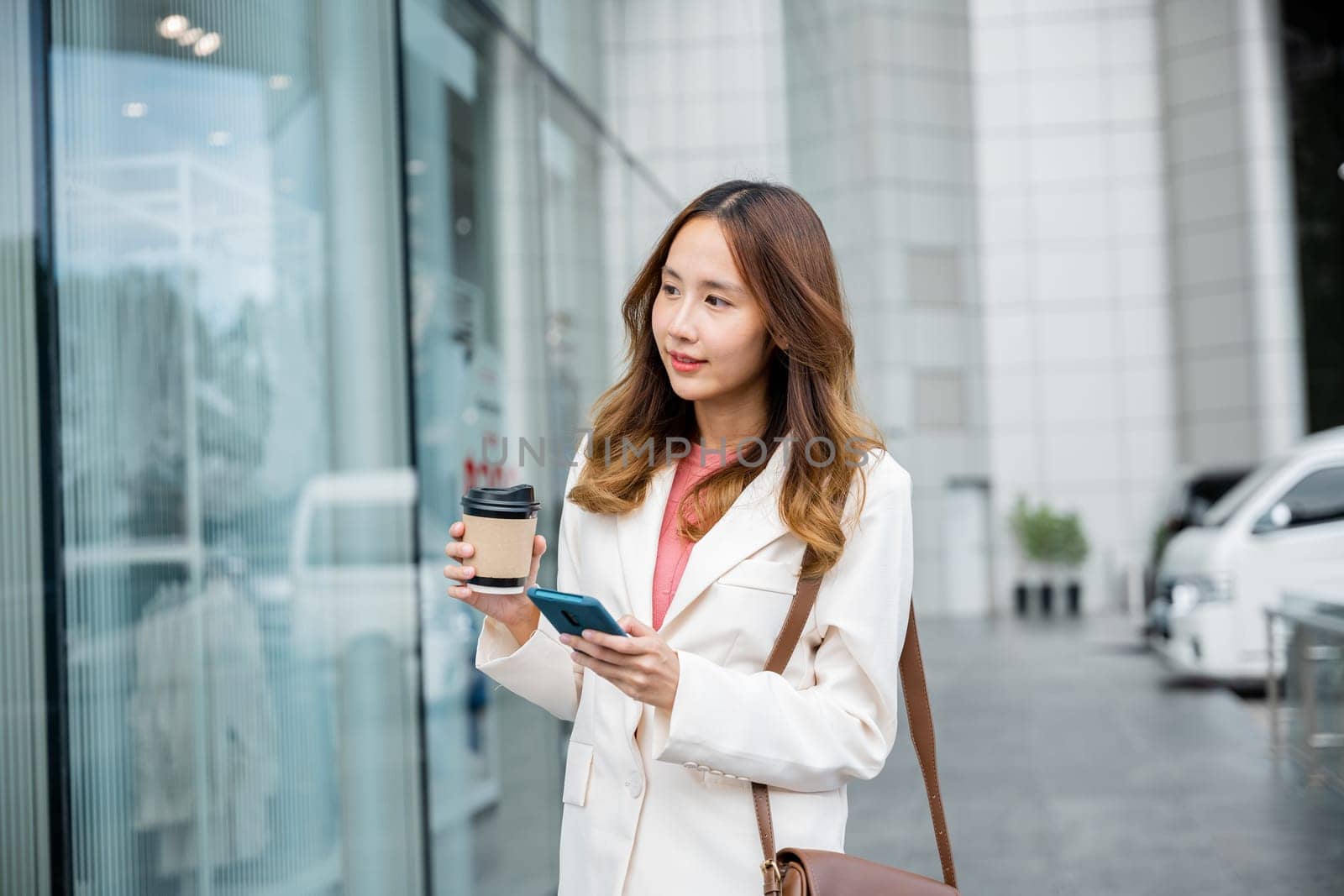 Professional woman on-the-go, managing work and coffee with ease using her smartphone and multitasking skills.