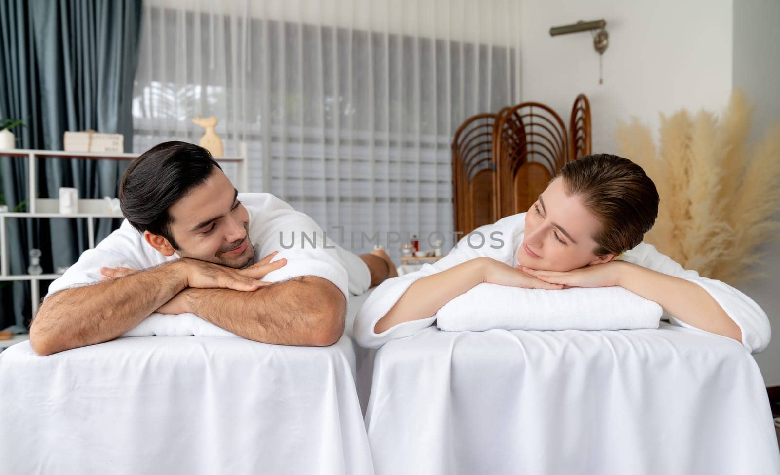 Caucasian couple customer enjoying relaxing anti-stress spa massage and pampering with beauty skin recreation leisure in day light ambient salon spa at luxury resort or hotel. Quiescent