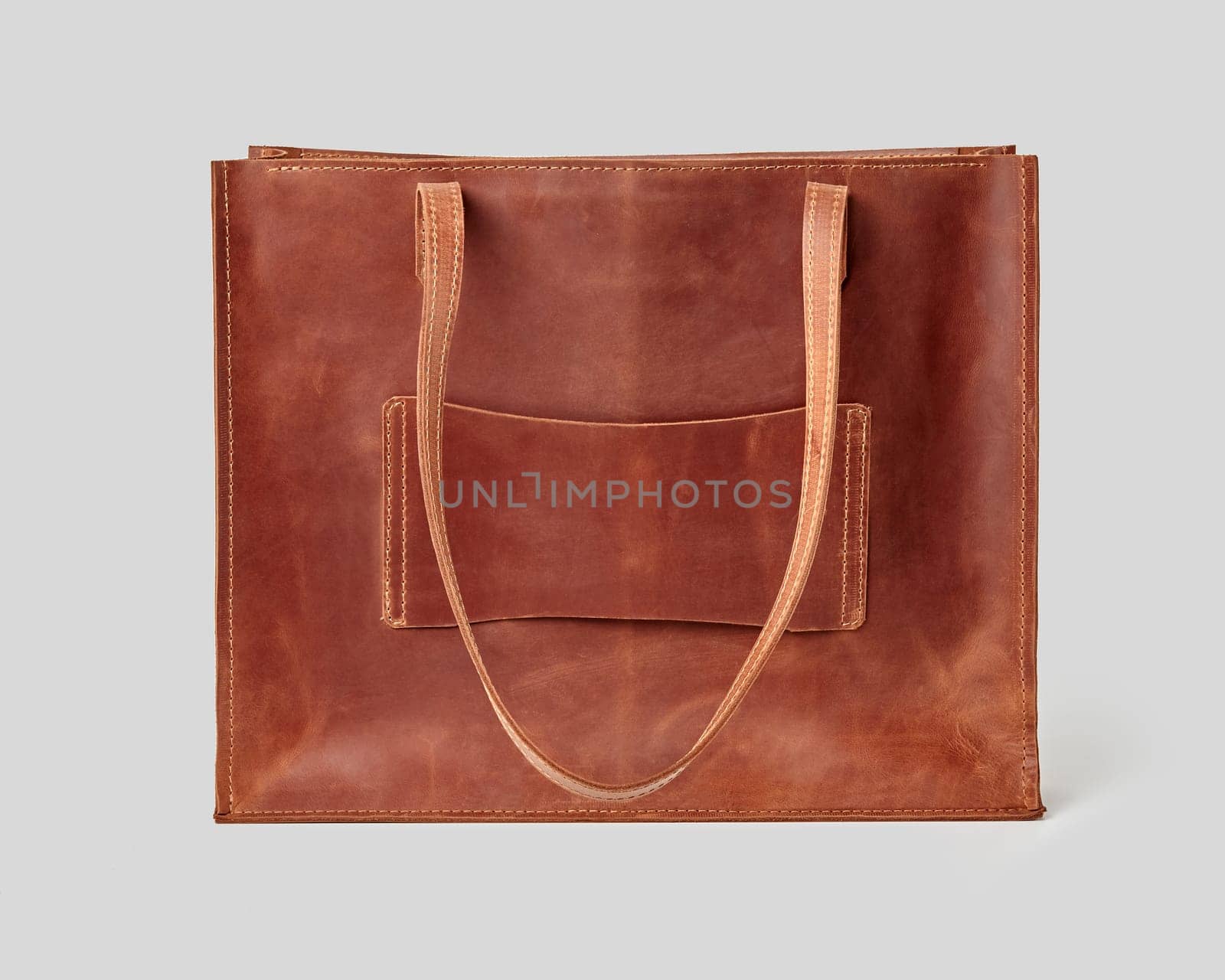 Classic brown leather tote bag featuring simple design with long handles against neutral grey backdrop. Women accessories concept