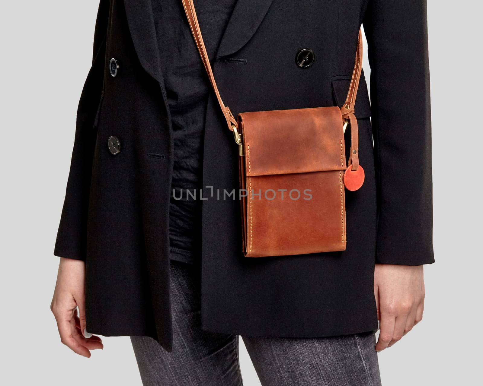 Fashionable brown leather crossbody messenger bag with motivational slogan on label tag complementing stylish look of young woman in casual black jacket and jeans