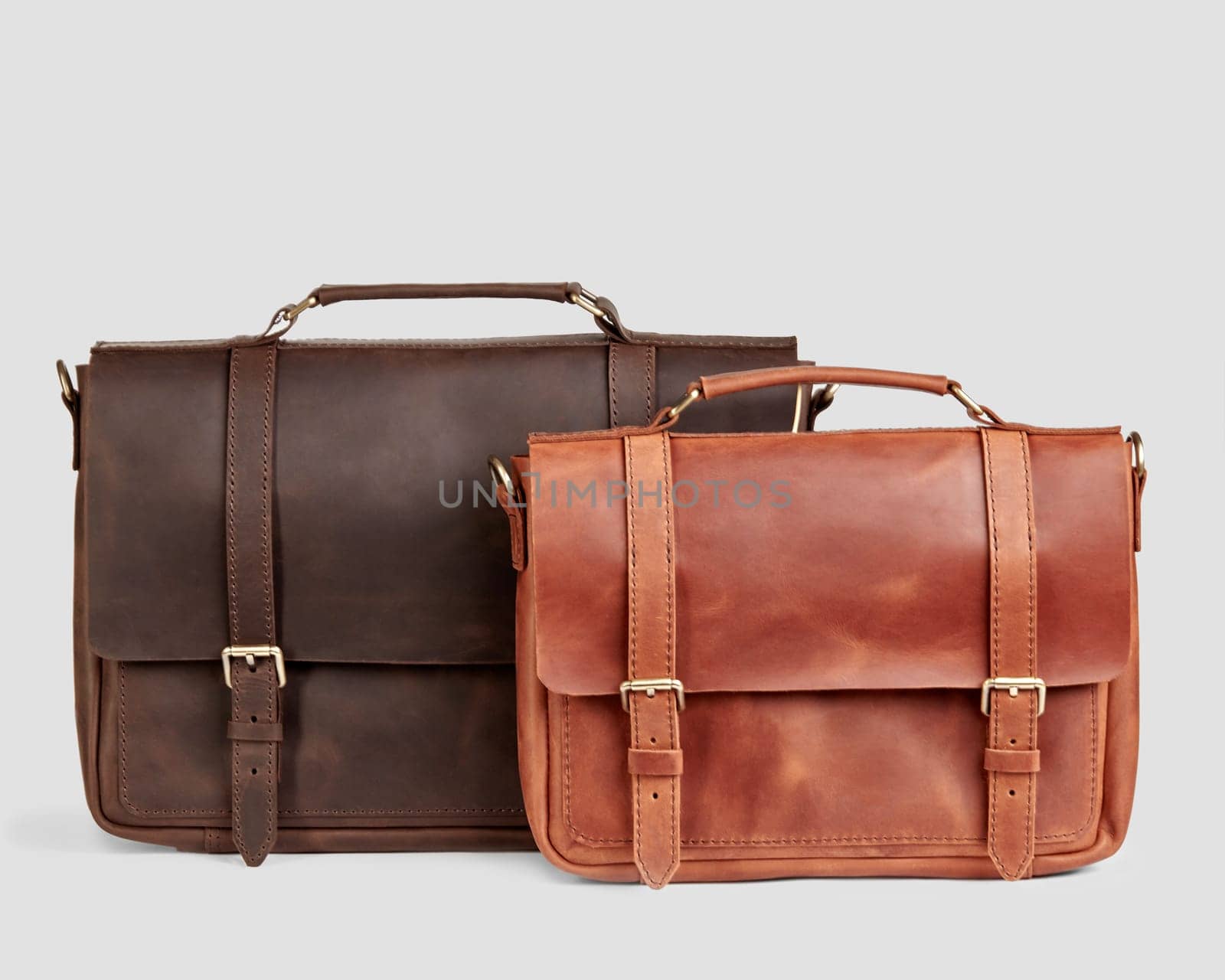 Stylish comfortable dark brown and copper colored leather messenger bags of different sizes with embossed initials, presented on light backdrop