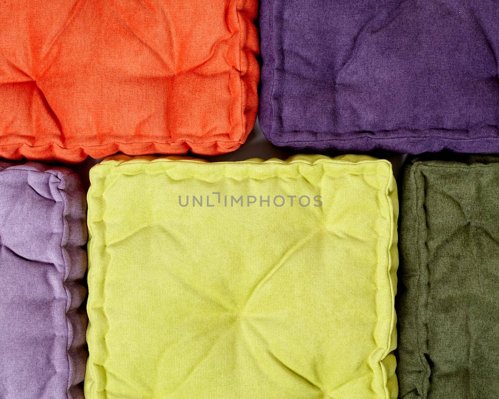Top-down perspective of neatly arranged velour quilted cushions in bright orange, purple, yellow, and green. Handcrafted accessories for comfort and stylish interior design