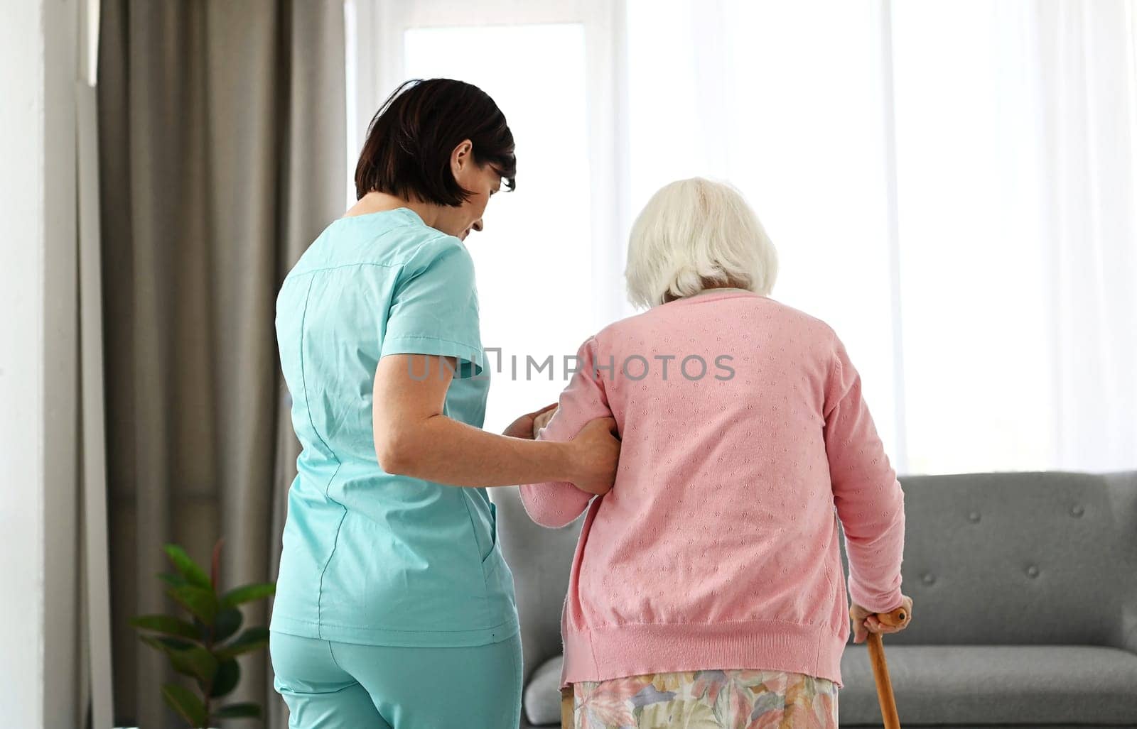 Nurse Assists Elderly Woman Moving Around Room by GekaSkr