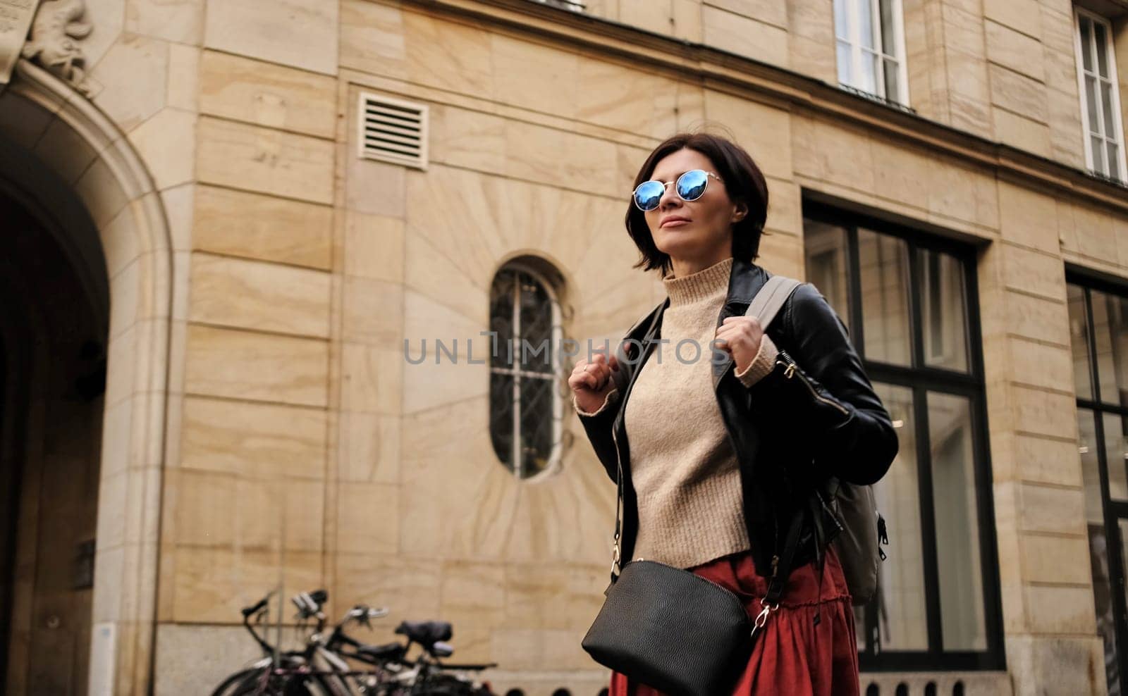 Stylish Woman With Sunglasses And Backpack Strolls In City by GekaSkr