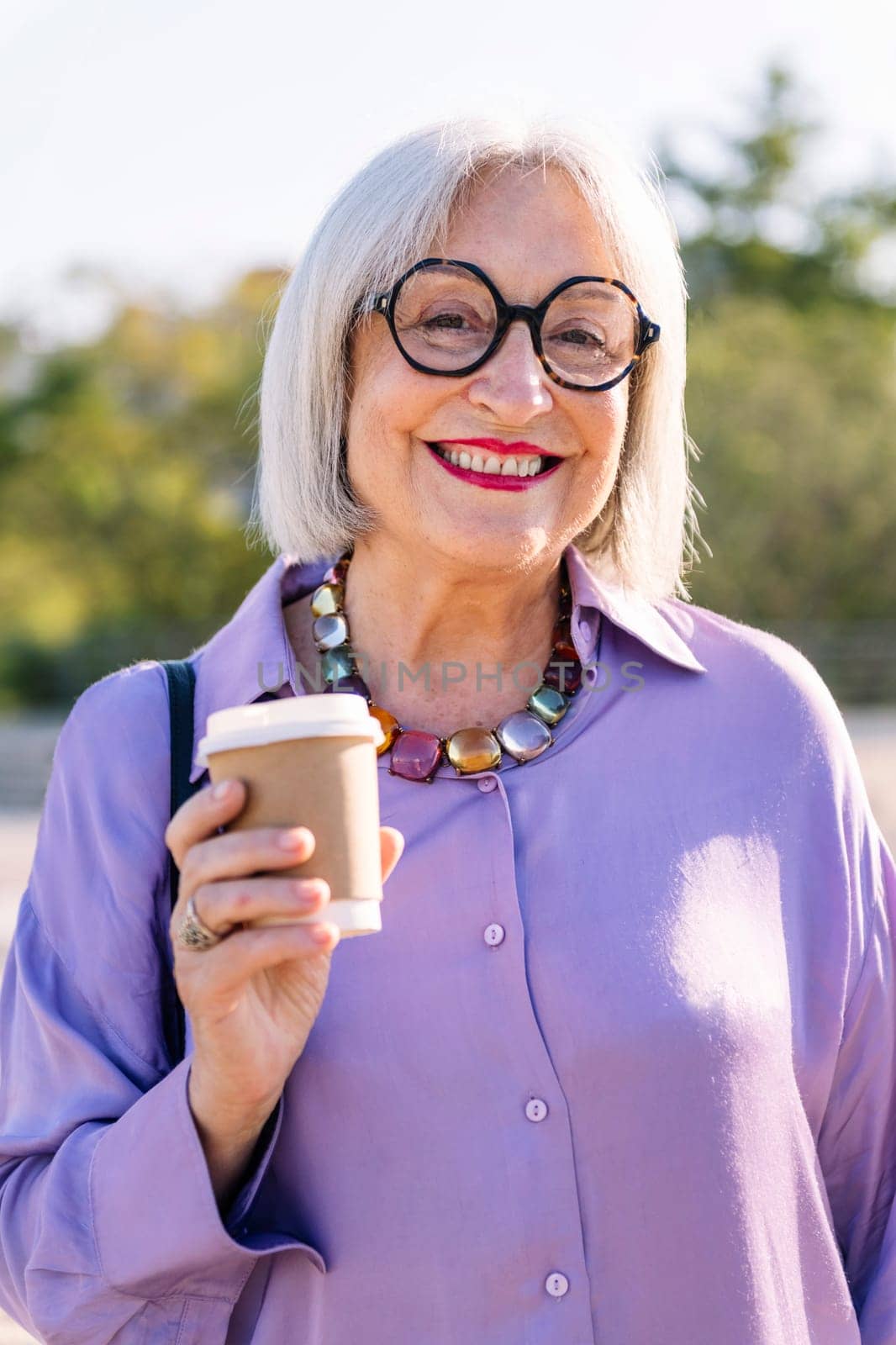 portrait of a smiling senior woman looking at camera with a takeaway coffee, concept of elderly people leisure and active lifestyle, copy space for text