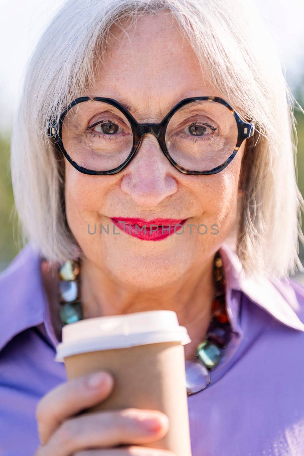 close up portrait of a smiling senior woman looking at camera with a takeaway coffee, concept of elderly people leisure and active lifestyle, copy space for text