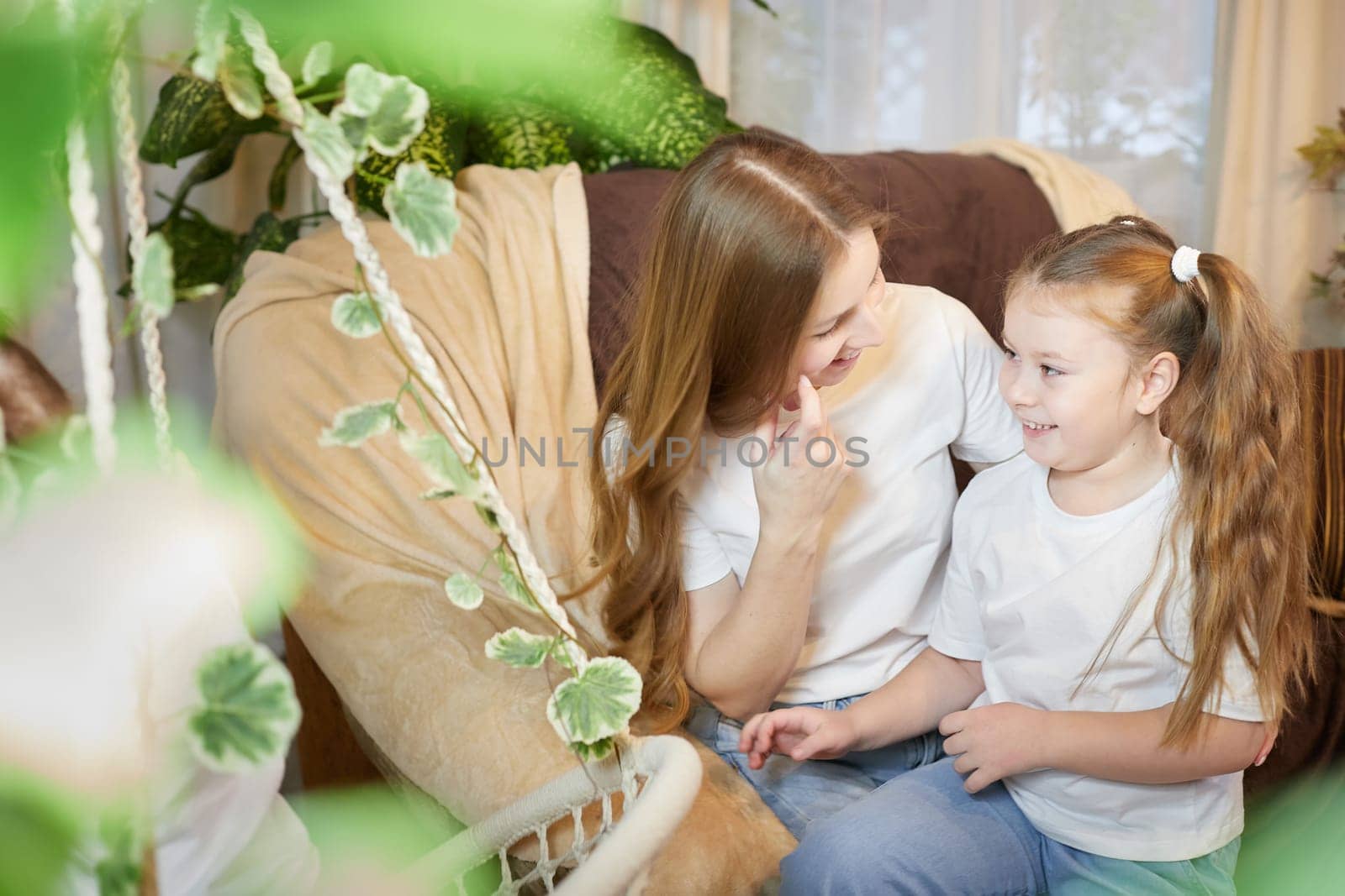 Happy loving family. Mother and her daughter child girl playing and hugging in living room with wicker chair by keleny