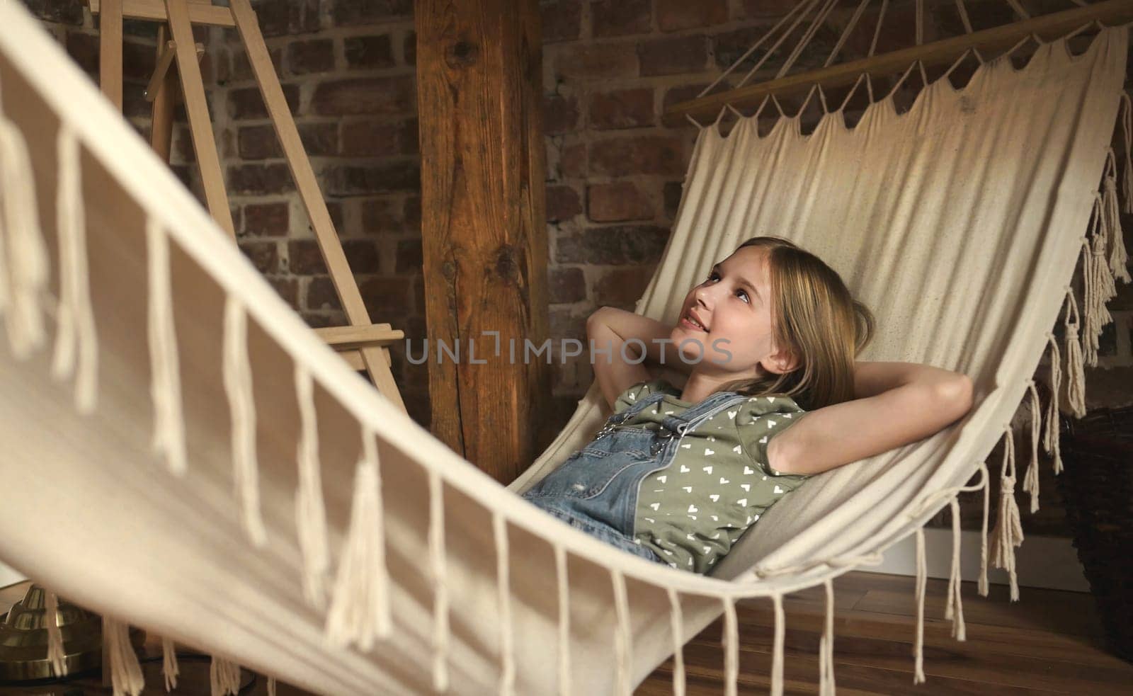 Preteen child girl lying in hammock in loft room at home. Pretty female kid enjoying summer vacation