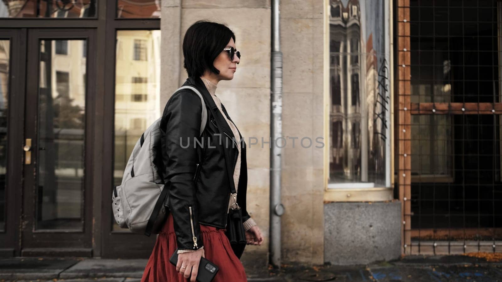 Attractive Woman In Sunglasses Walks By City Street With Backpack, Radiating Confidence And Style
