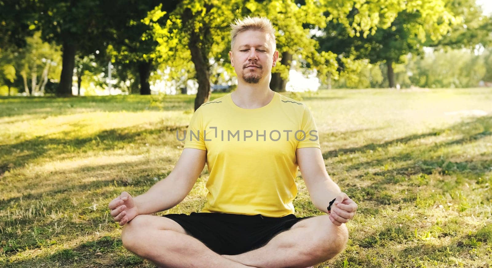 Young man sitting in Lotus position, practicing yoga and meditation outdoors by GekaSkr