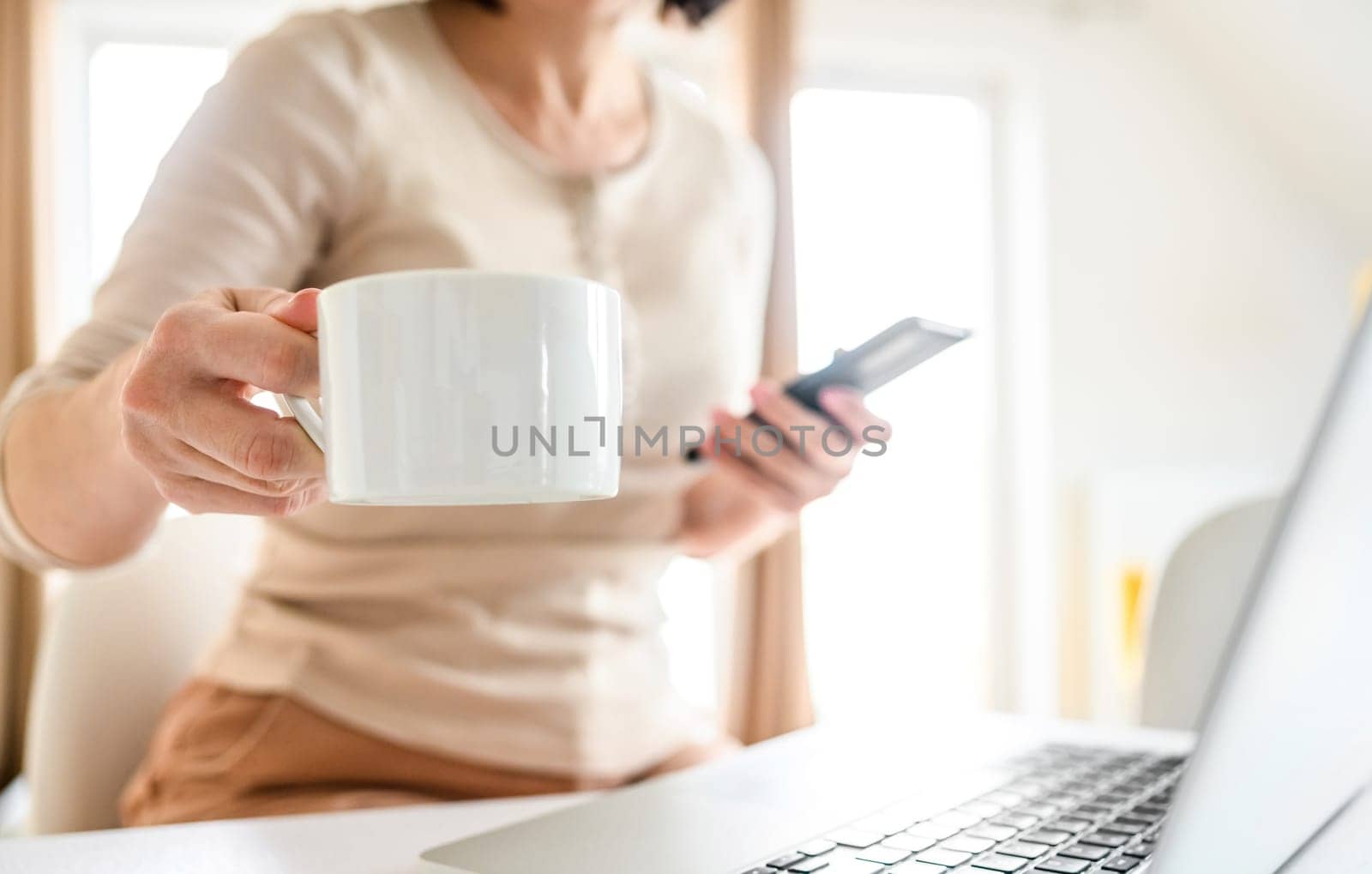 Girl drinking fresh morning coffee at the kitchen and using smartphone, morning social media checking