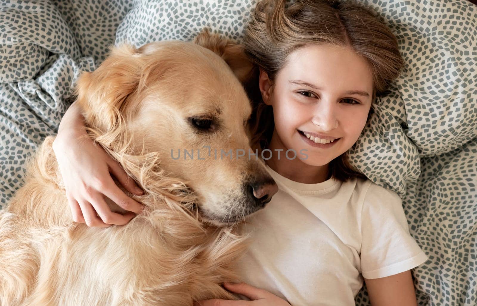 Happy Little Girl Hugging Golden Retriever Dog And Smiling Lying On A Bed