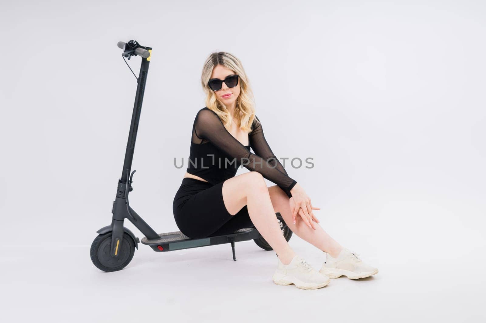 A blonde woman on a red background sitting on electro scooter and resting, copy space